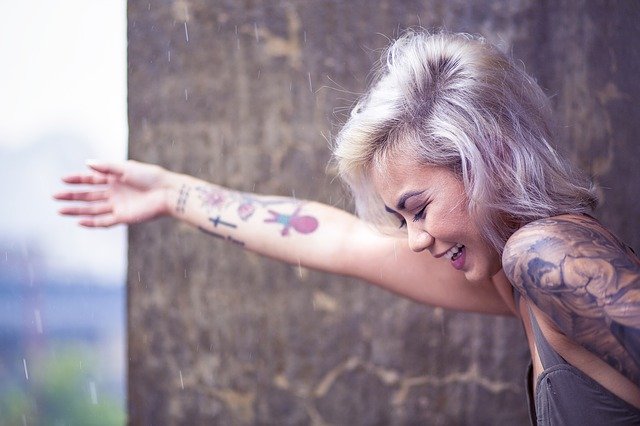 Žena s farebnými vlasmi a tetovaním sa smeje 